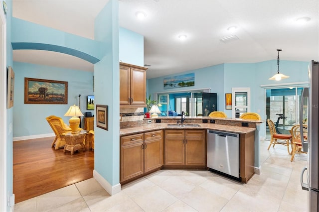 kitchen featuring a sink, hanging light fixtures, appliances with stainless steel finishes, brown cabinets, and plenty of natural light