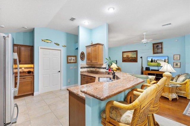 kitchen with freestanding refrigerator, brown cabinetry, a sink, and visible vents