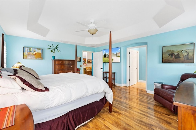 bedroom featuring a ceiling fan, baseboards, a tray ceiling, and wood finished floors