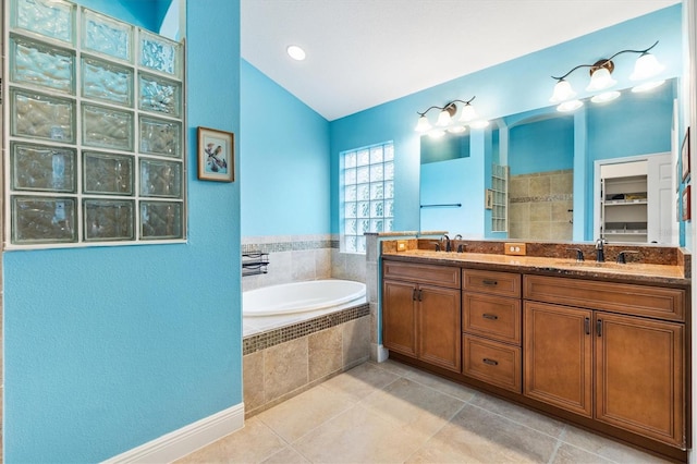 bathroom with double vanity, lofted ceiling, tile patterned floors, a garden tub, and a sink