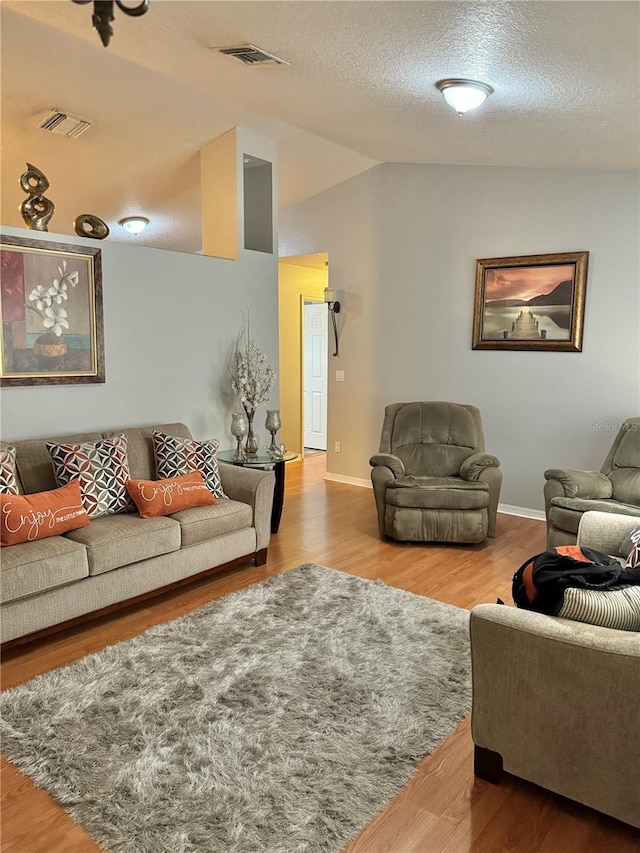 living room with hardwood / wood-style flooring, vaulted ceiling, and a textured ceiling