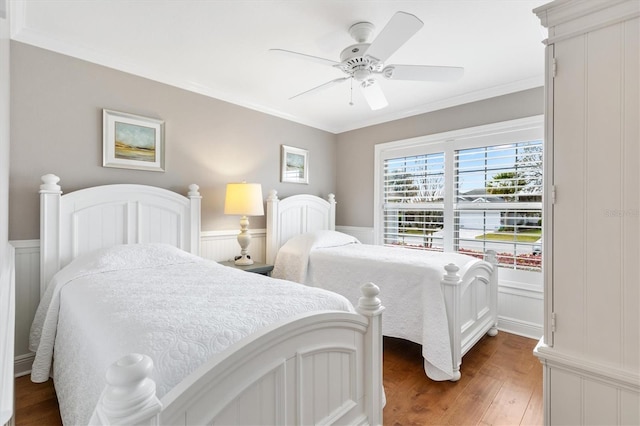 bedroom with crown molding, dark wood-style floors, wainscoting, and a ceiling fan