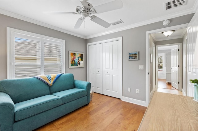 living area with baseboards, visible vents, light wood-style flooring, and crown molding