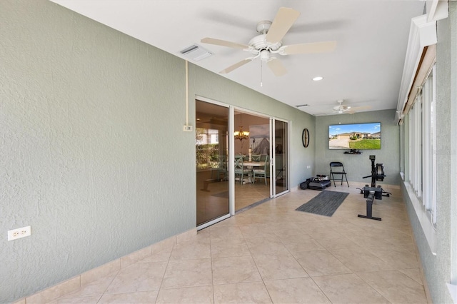 exercise room featuring ceiling fan with notable chandelier, visible vents, light tile patterned floors, and a textured wall