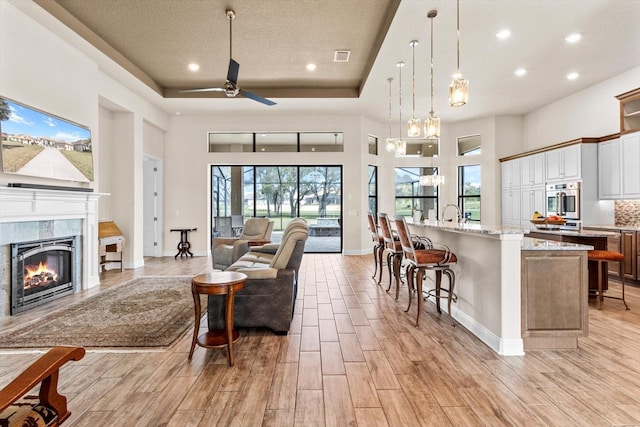 living room featuring a towering ceiling, a tile fireplace, light hardwood / wood-style floors, ceiling fan, and a textured ceiling