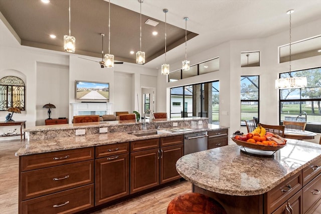 kitchen with stainless steel dishwasher, a kitchen island with sink, light stone counters, and a raised ceiling