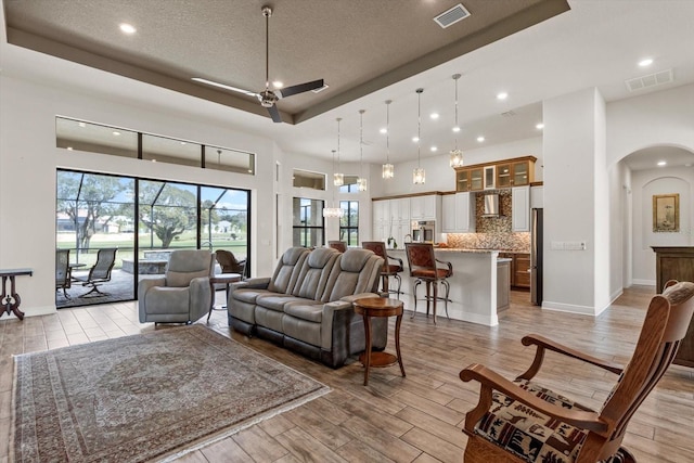 living room featuring ceiling fan, light hardwood / wood-style floors, a raised ceiling, and a textured ceiling