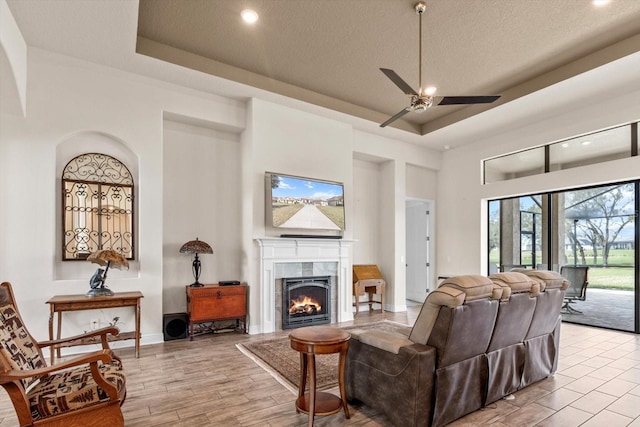 living room with a tile fireplace, a textured ceiling, ceiling fan, light hardwood / wood-style floors, and a tray ceiling