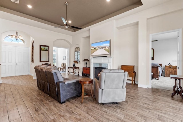 living room with a fireplace, a raised ceiling, and ceiling fan with notable chandelier