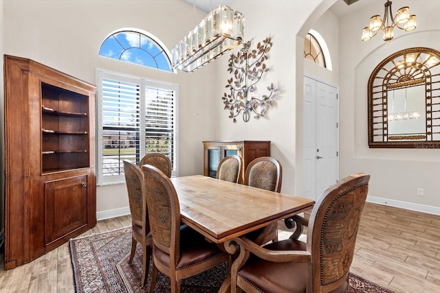 dining space featuring a towering ceiling, a notable chandelier, and light hardwood / wood-style flooring