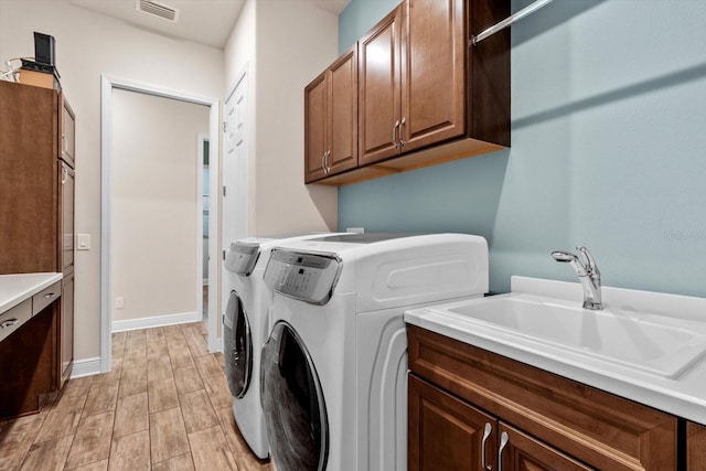 laundry room featuring washing machine and dryer, sink, cabinets, and light wood-type flooring