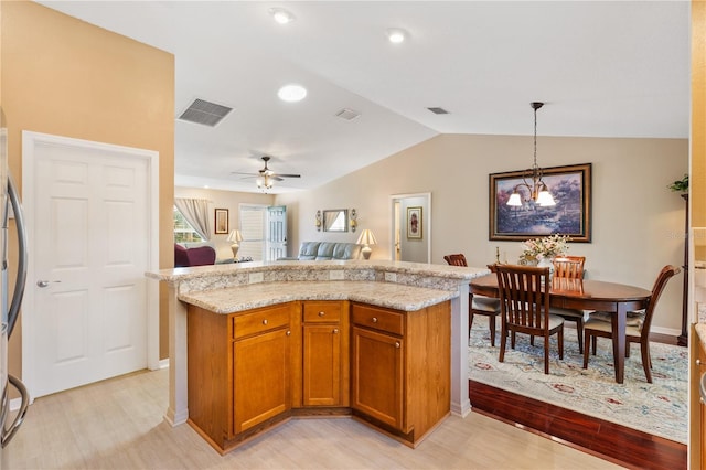 kitchen featuring vaulted ceiling, open floor plan, light wood-type flooring, brown cabinetry, and pendant lighting