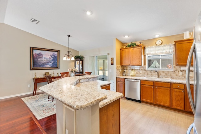 kitchen featuring appliances with stainless steel finishes, brown cabinetry, vaulted ceiling, a sink, and a kitchen island