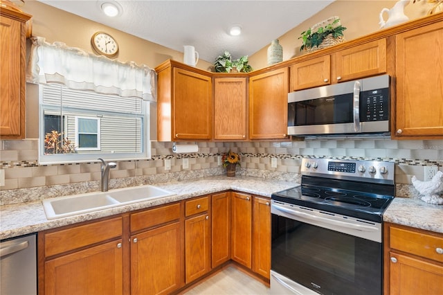 kitchen featuring brown cabinetry, appliances with stainless steel finishes, decorative backsplash, and a sink