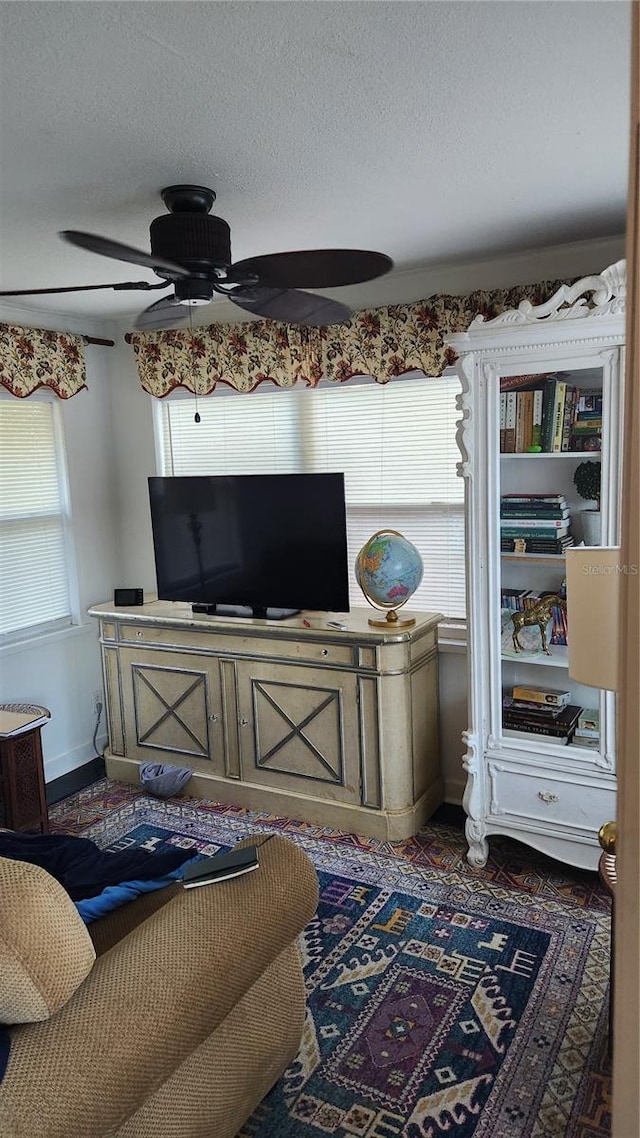 living area featuring a textured ceiling, a ceiling fan, and baseboards