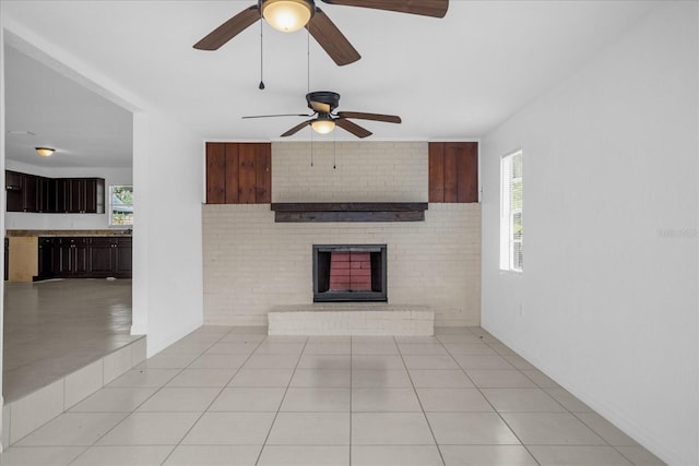 unfurnished living room featuring light tile patterned flooring, brick wall, a fireplace, and a wealth of natural light