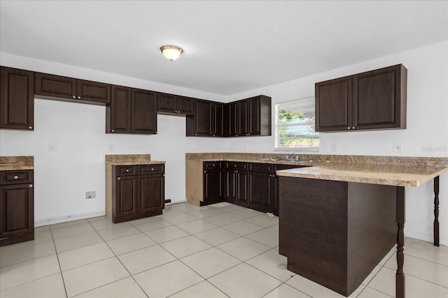 kitchen with a kitchen bar, light tile patterned floors, dark brown cabinetry, and kitchen peninsula