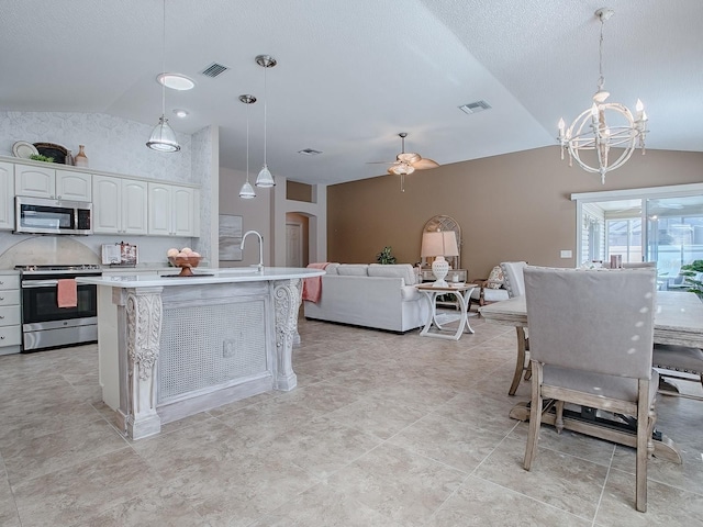 kitchen featuring lofted ceiling, white cabinetry, hanging light fixtures, an island with sink, and stainless steel appliances