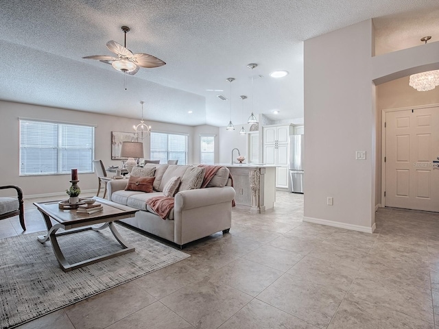 living room with lofted ceiling, sink, a textured ceiling, light tile patterned flooring, and ceiling fan with notable chandelier