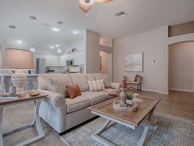 tiled living room featuring ceiling fan, lofted ceiling, and a textured ceiling