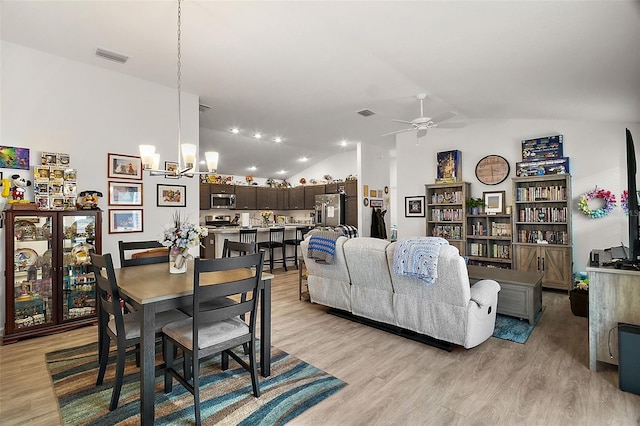 dining area featuring light wood-type flooring, lofted ceiling, and ceiling fan with notable chandelier