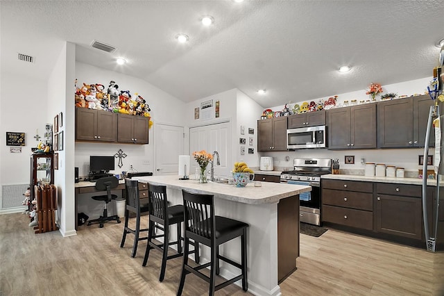 kitchen with a kitchen breakfast bar, stainless steel appliances, a kitchen island with sink, and dark brown cabinetry
