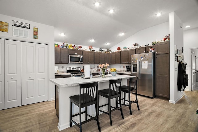 kitchen with a kitchen island with sink, dark brown cabinets, a kitchen bar, and stainless steel appliances