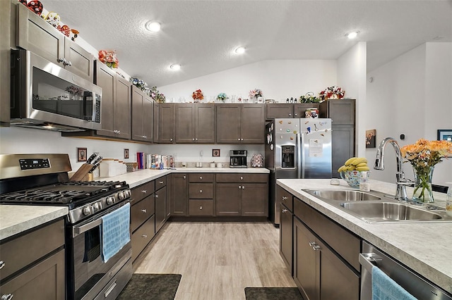 kitchen featuring lofted ceiling, light hardwood / wood-style floors, sink, a textured ceiling, and appliances with stainless steel finishes