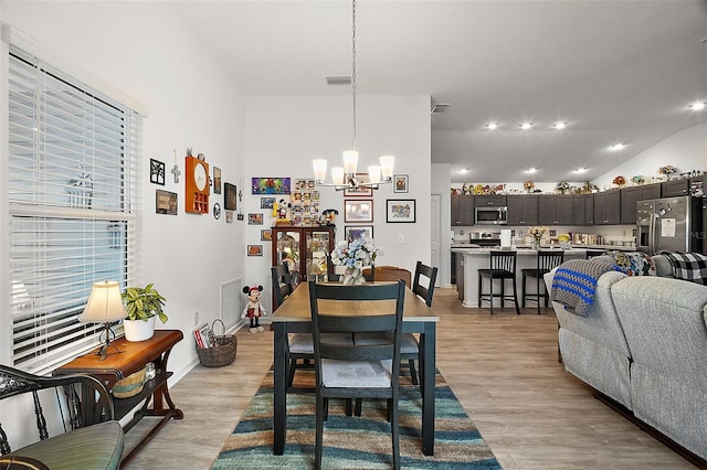 dining space with lofted ceiling, a chandelier, and light hardwood / wood-style flooring
