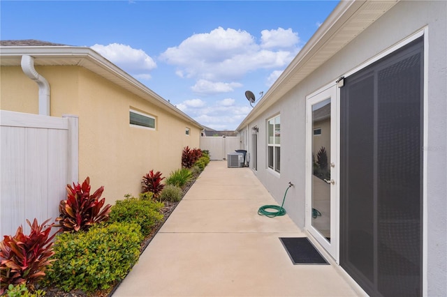 view of side of home featuring central AC unit, fence, a patio, and stucco siding