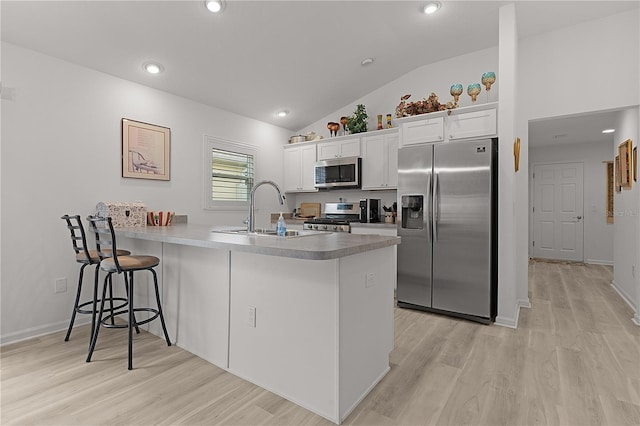 kitchen featuring stainless steel appliances, a peninsula, a kitchen bar, and white cabinetry