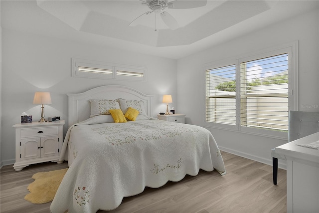 bedroom with light wood finished floors, a tray ceiling, and baseboards