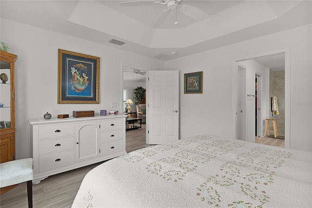 bedroom featuring light wood-type flooring, visible vents, a raised ceiling, and a ceiling fan