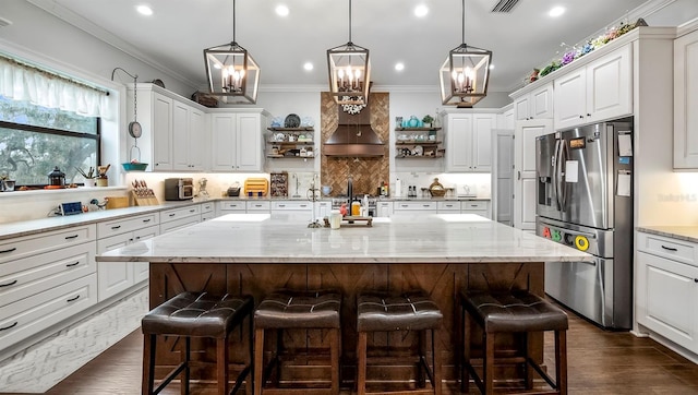 kitchen featuring light stone counters, white cabinetry, a kitchen breakfast bar, a kitchen island, and stainless steel fridge