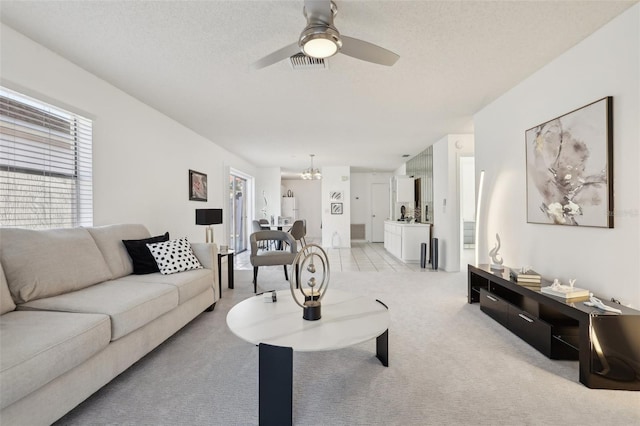 living area with light colored carpet, visible vents, a textured ceiling, and ceiling fan with notable chandelier