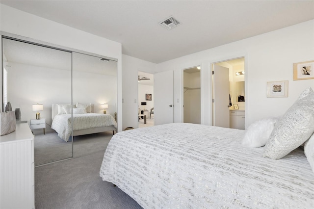 bedroom with dark colored carpet, a closet, visible vents, and ensuite bath