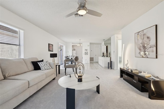 living room with visible vents, a textured ceiling, light colored carpet, and ceiling fan with notable chandelier