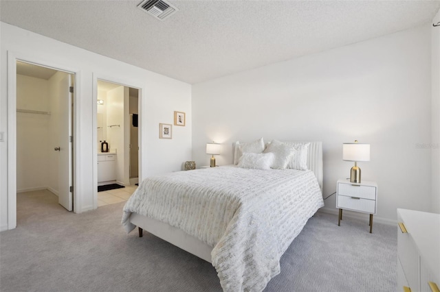 bedroom with baseboards, visible vents, a textured ceiling, a walk in closet, and light carpet