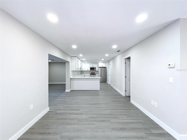 kitchen with appliances with stainless steel finishes, hardwood / wood-style floors, white cabinets, and kitchen peninsula