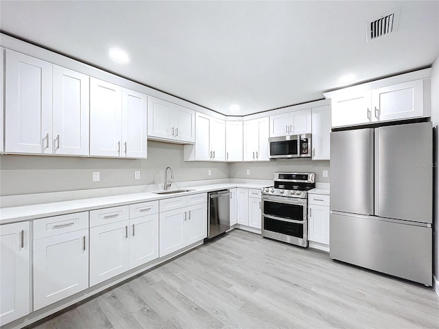 kitchen featuring appliances with stainless steel finishes, sink, light hardwood / wood-style flooring, and white cabinets