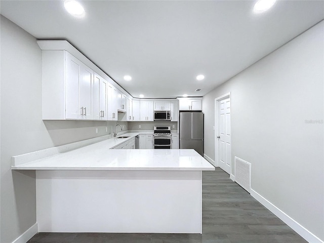 kitchen with appliances with stainless steel finishes, kitchen peninsula, sink, and white cabinets