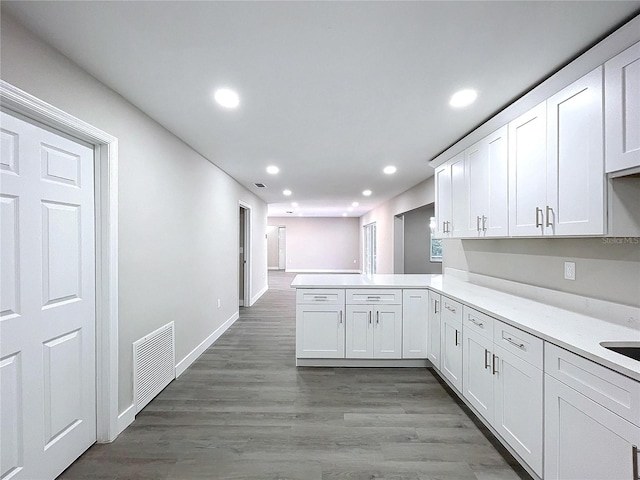 kitchen featuring hardwood / wood-style flooring, kitchen peninsula, and white cabinets