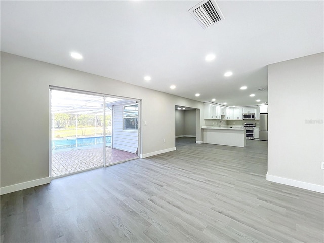 unfurnished living room featuring sink and light hardwood / wood-style floors