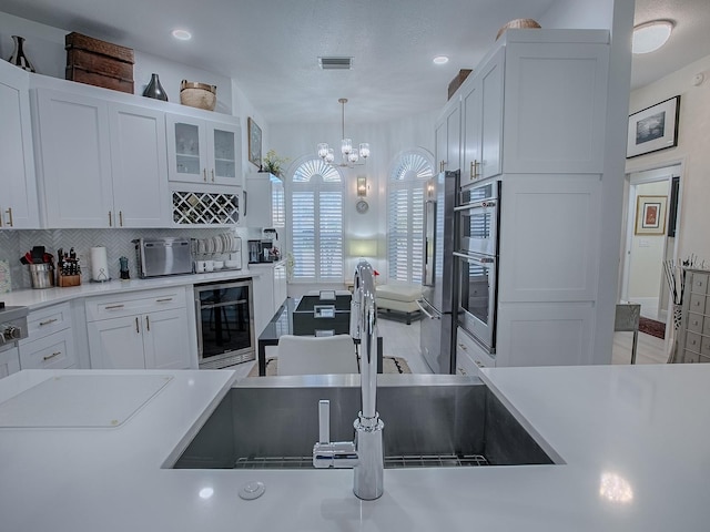 kitchen featuring light countertops, hanging light fixtures, glass insert cabinets, white cabinetry, and a sink