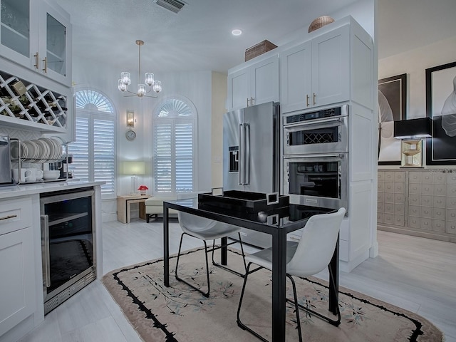 kitchen featuring beverage cooler, stainless steel appliances, white cabinets, light countertops, and glass insert cabinets