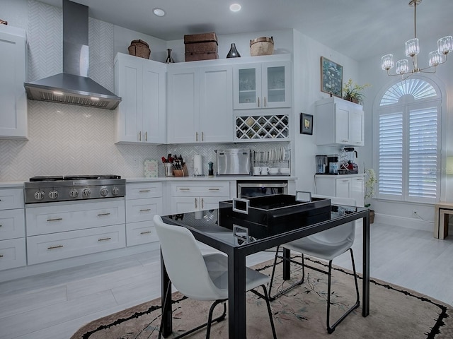 kitchen featuring white cabinetry, wall chimney exhaust hood, glass insert cabinets, and light countertops