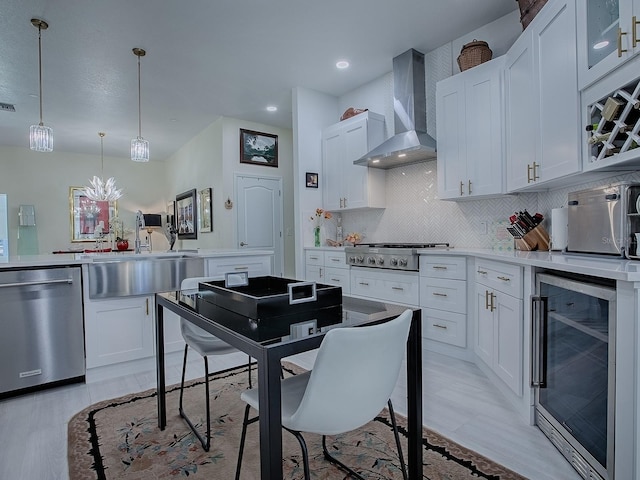 kitchen with beverage cooler, appliances with stainless steel finishes, wall chimney range hood, and white cabinets