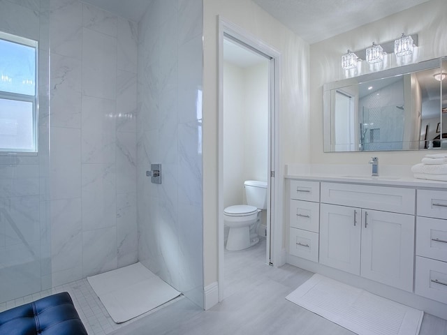 full bathroom featuring tiled shower, vanity, and toilet