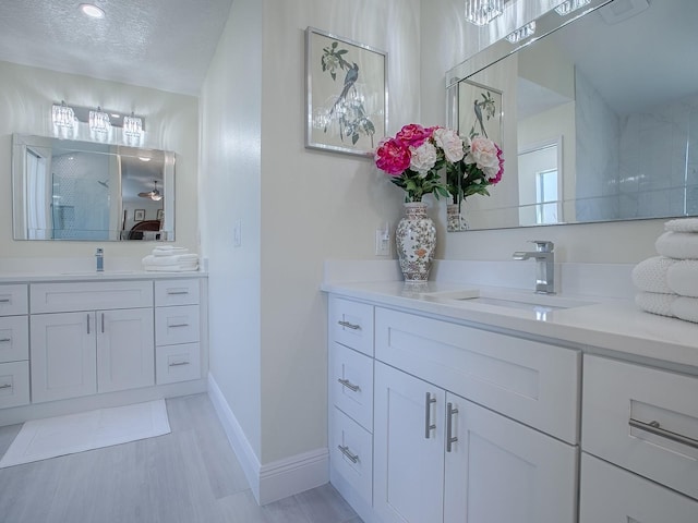 bathroom featuring a textured ceiling, baseboards, two vanities, and a sink