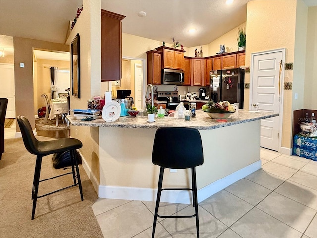 kitchen featuring a breakfast bar area, stainless steel appliances, light stone counters, light tile patterned flooring, and vaulted ceiling